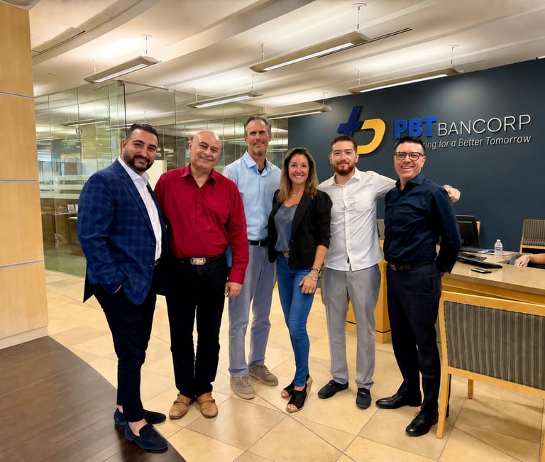 Six professionals posing together in a modern office with Bancorp branding on the wall behind them